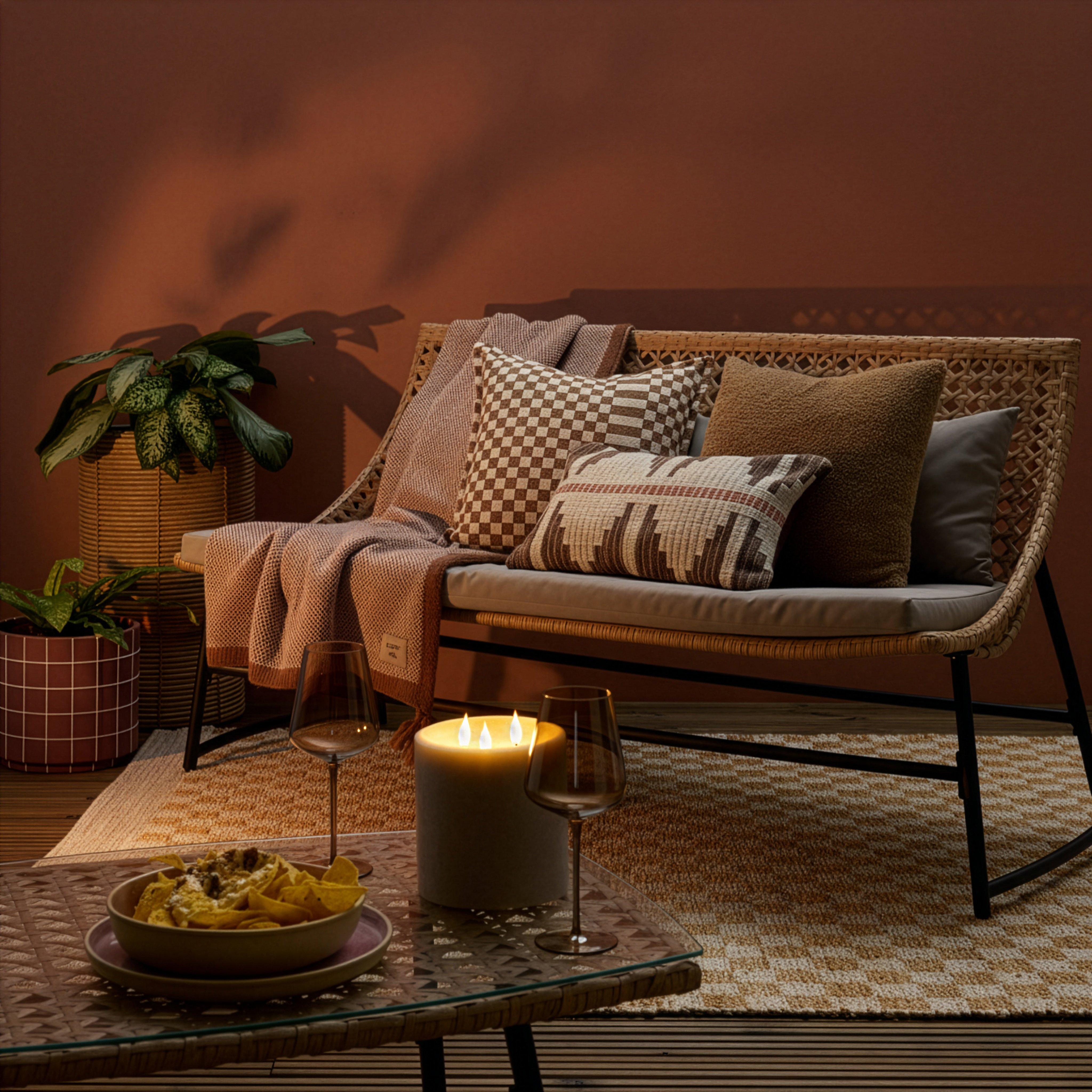 Softly lit garden with rattan sofa set. The sofa is decorated with throws and a range of outdoor cushions, creating a warm inviting outdoor space.