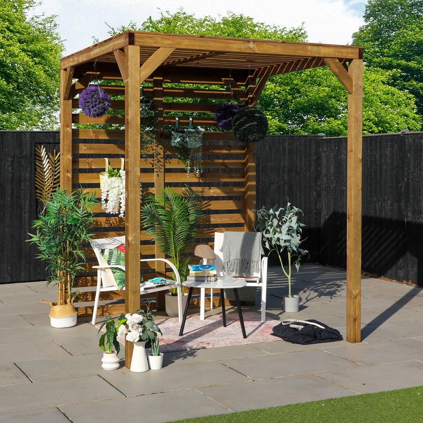 A garden pergola with a wooden lattice pattern, surrounded by lush potted plants and hanging flowers. Two chairs with blankets and books create a relaxing atmosphere.