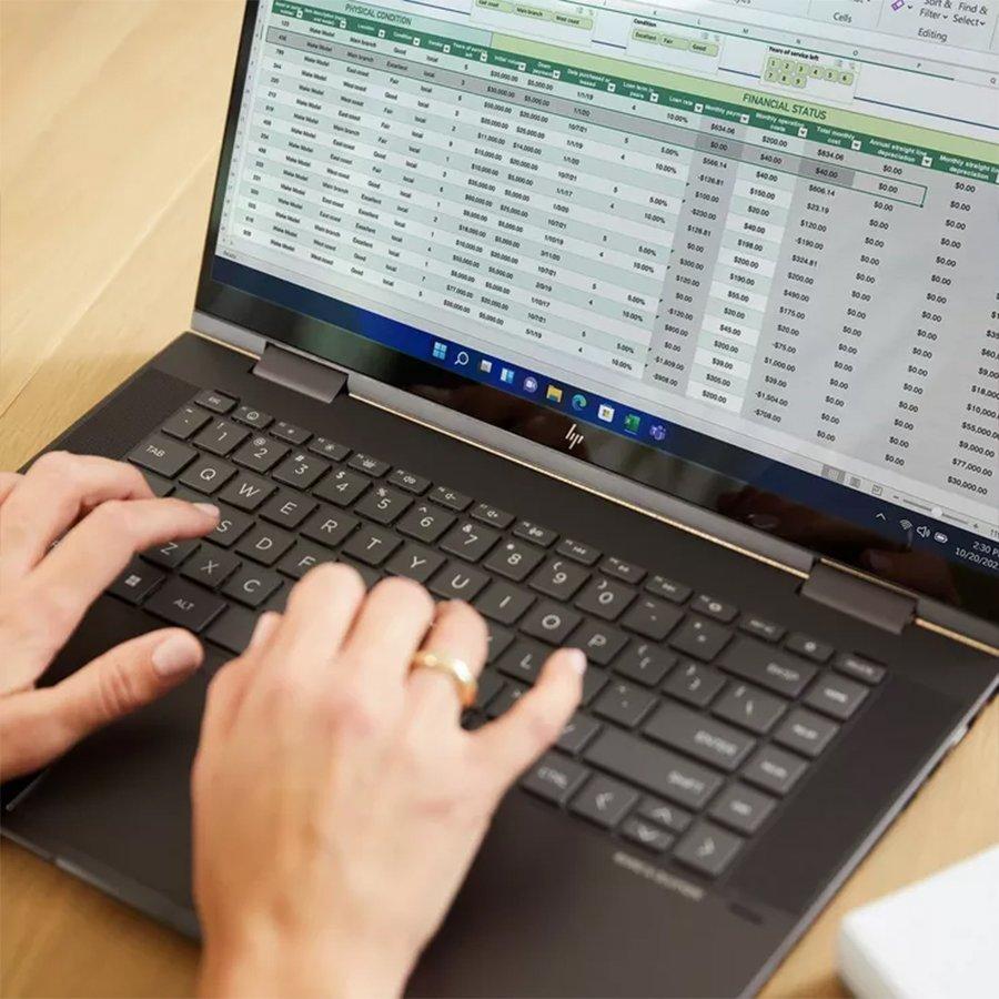 Woman typing on clean black laptop keyboard with a data filled spreadsheet visible on the screen.