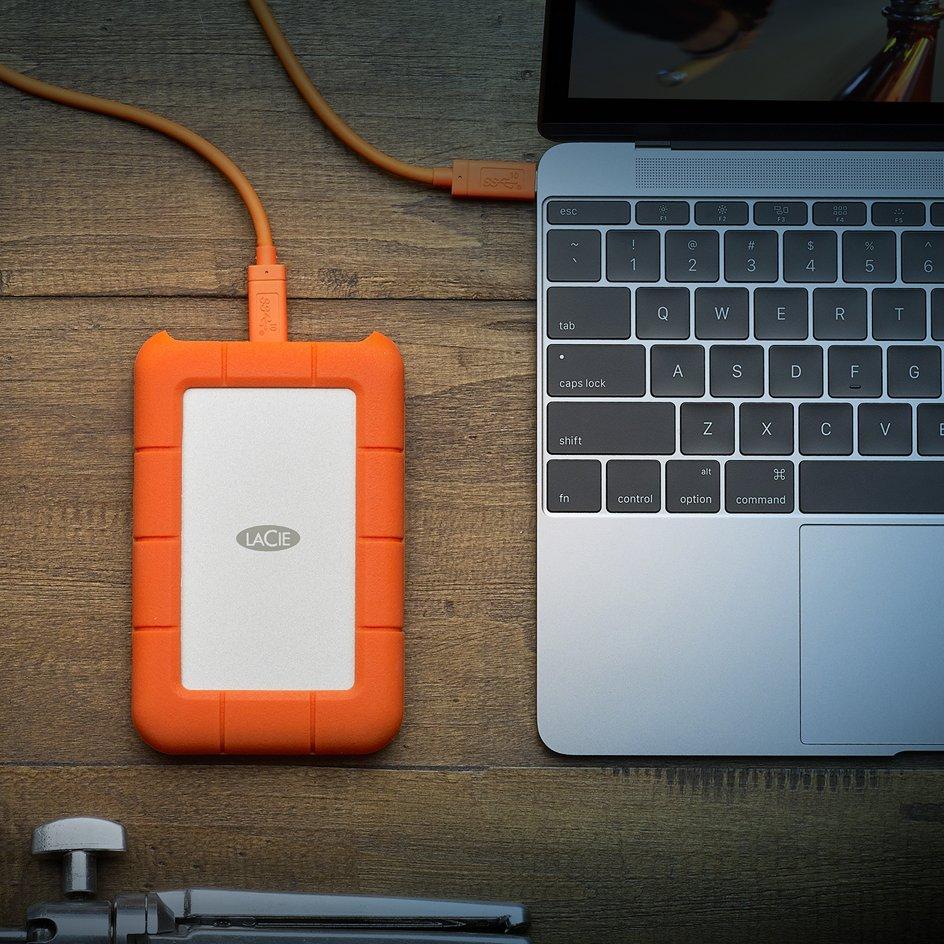 Orange portable hardrive is plugged into a silver laptop.