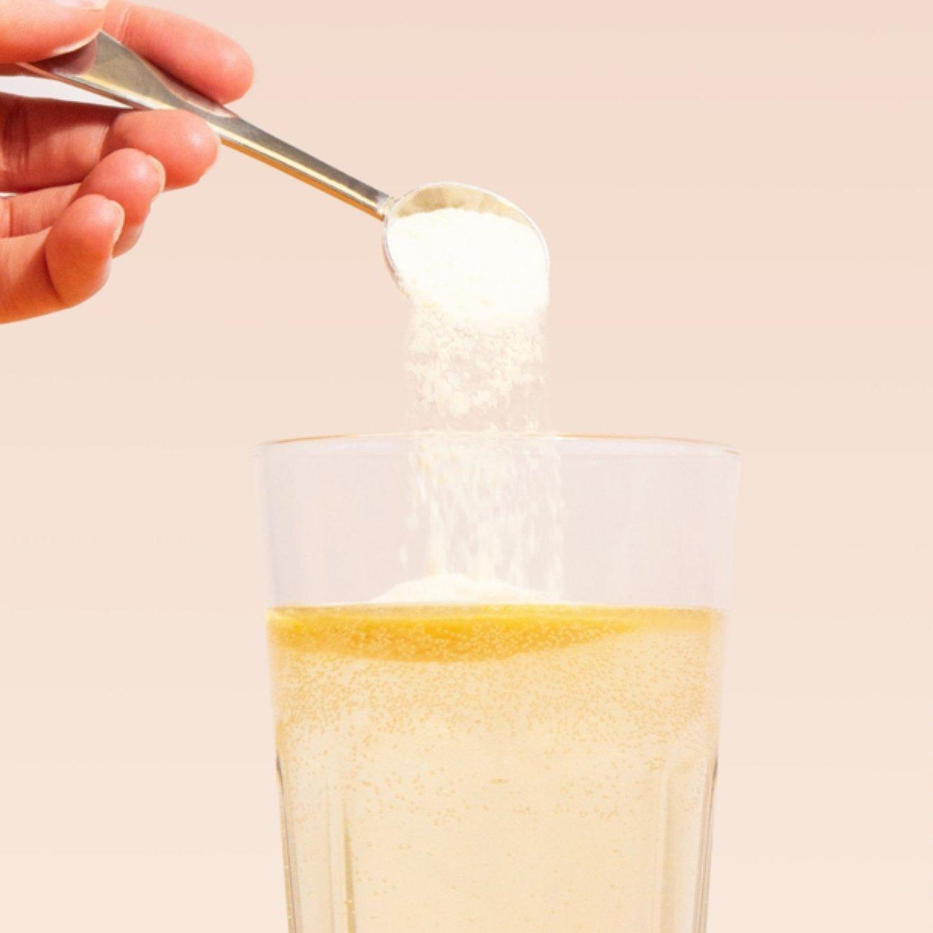Someone sprinkling collagen powder into a glass of water