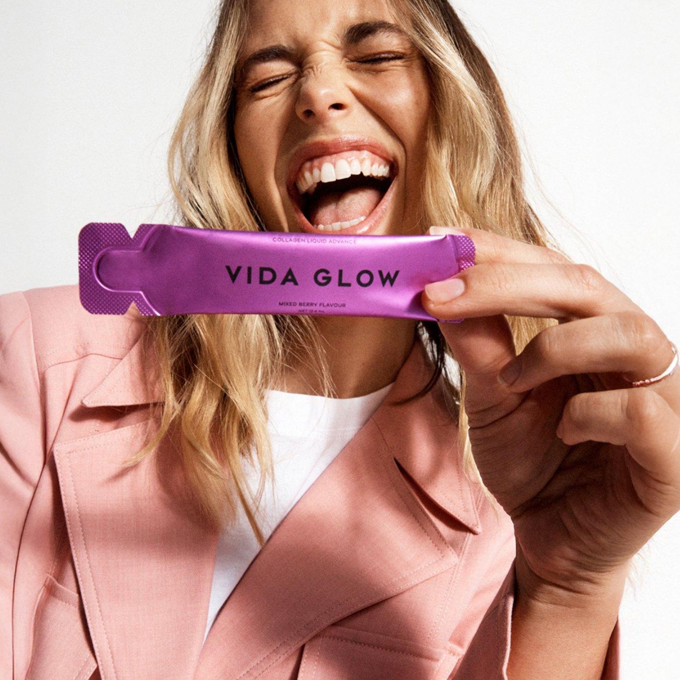 Model smiling excitedly while holding a sachet of Vida Glow's liquid collagen