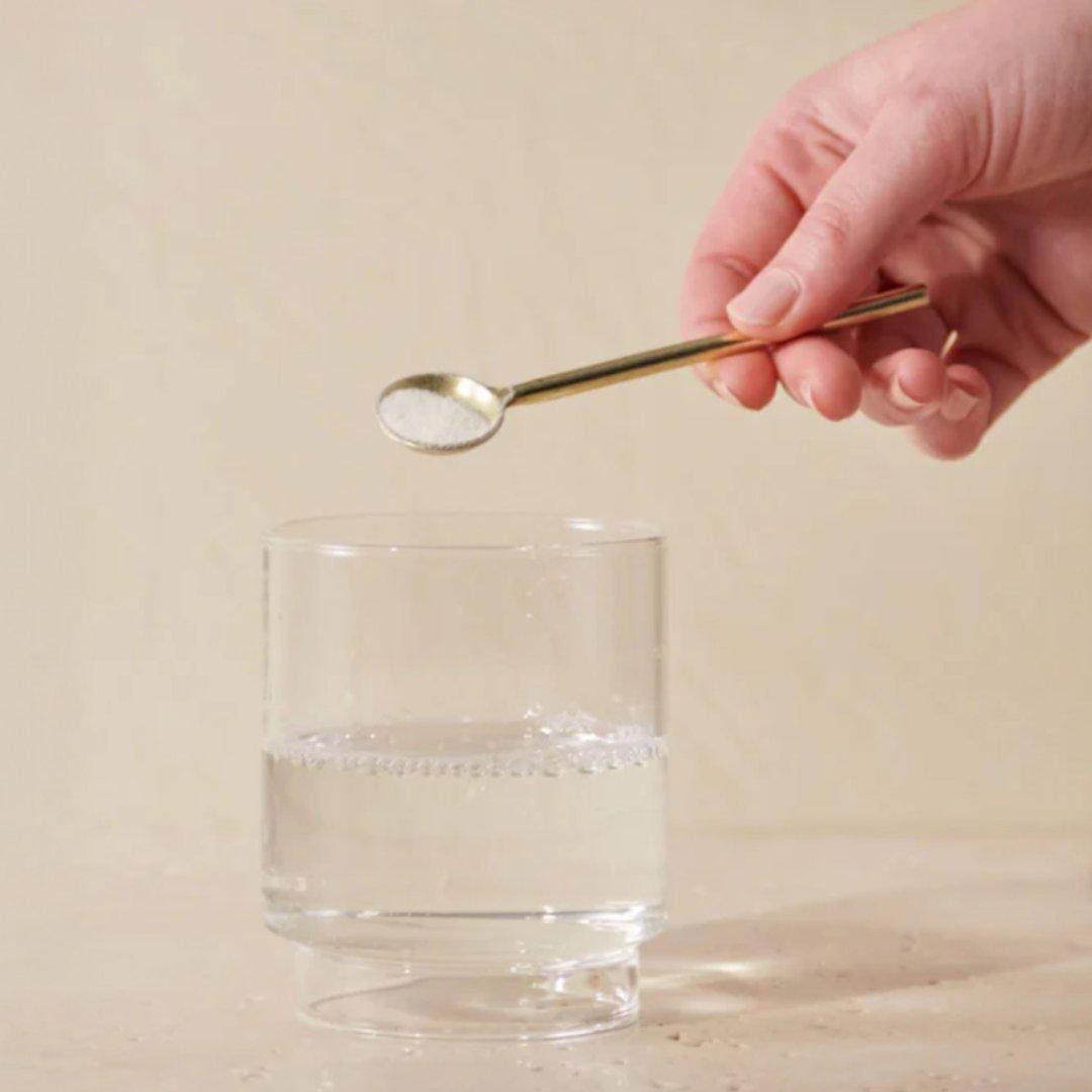 Glass of water with someone dropping a spoonful of collagen powder into it