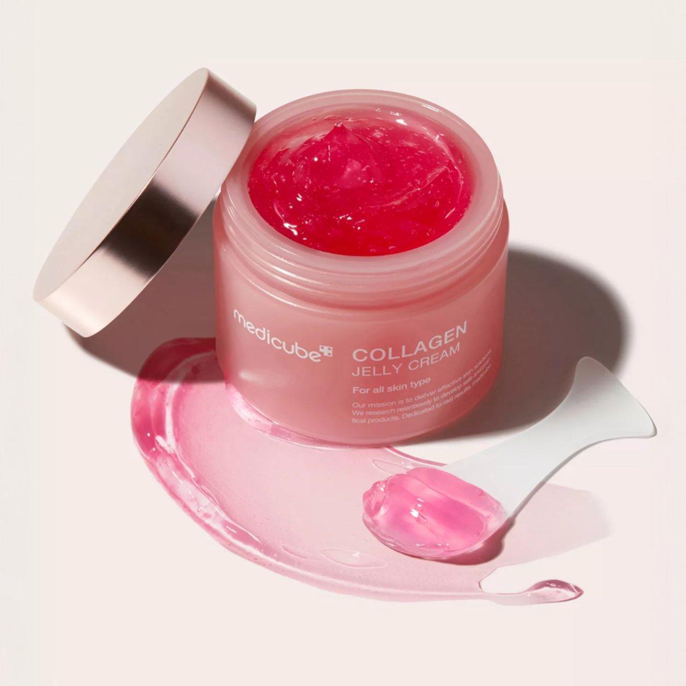 Pot of the Medicube Collagen Jelly Cream with the lid off - showing the pink jelly cream inside. A small spatula with the product on it is next to the container.