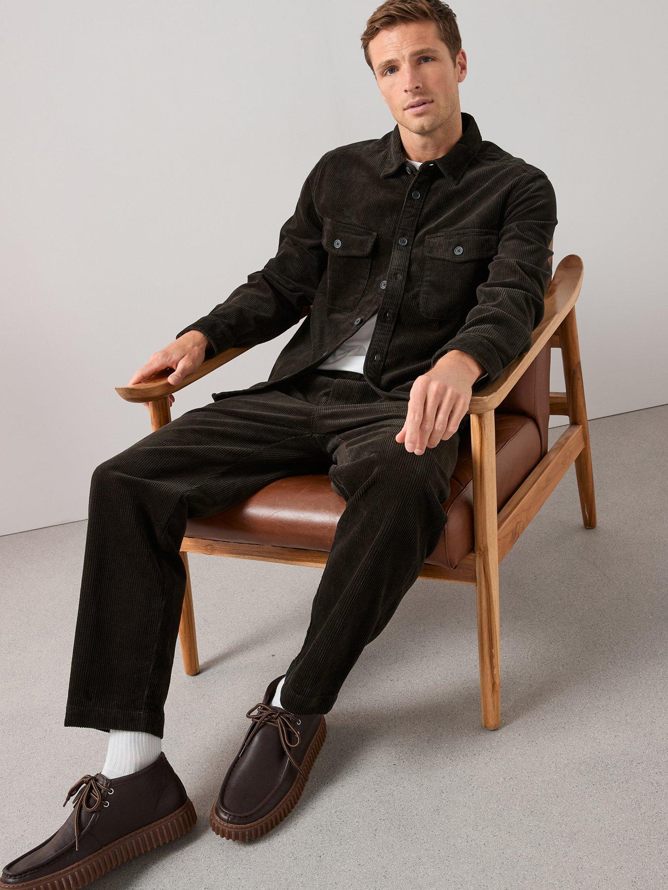 Model sitting casually on a chair with his legs stretched out to show off the brown corduroy trousers. He's wearing a matching brown cord shirt and some brown shoes. 
