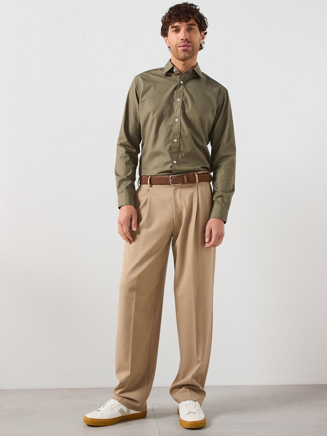 Man wearing a khaki buttoned up shirt tucked into loose-fit beige trousers and trainers. A modern take on a smart causal Christmas outfit for men.
