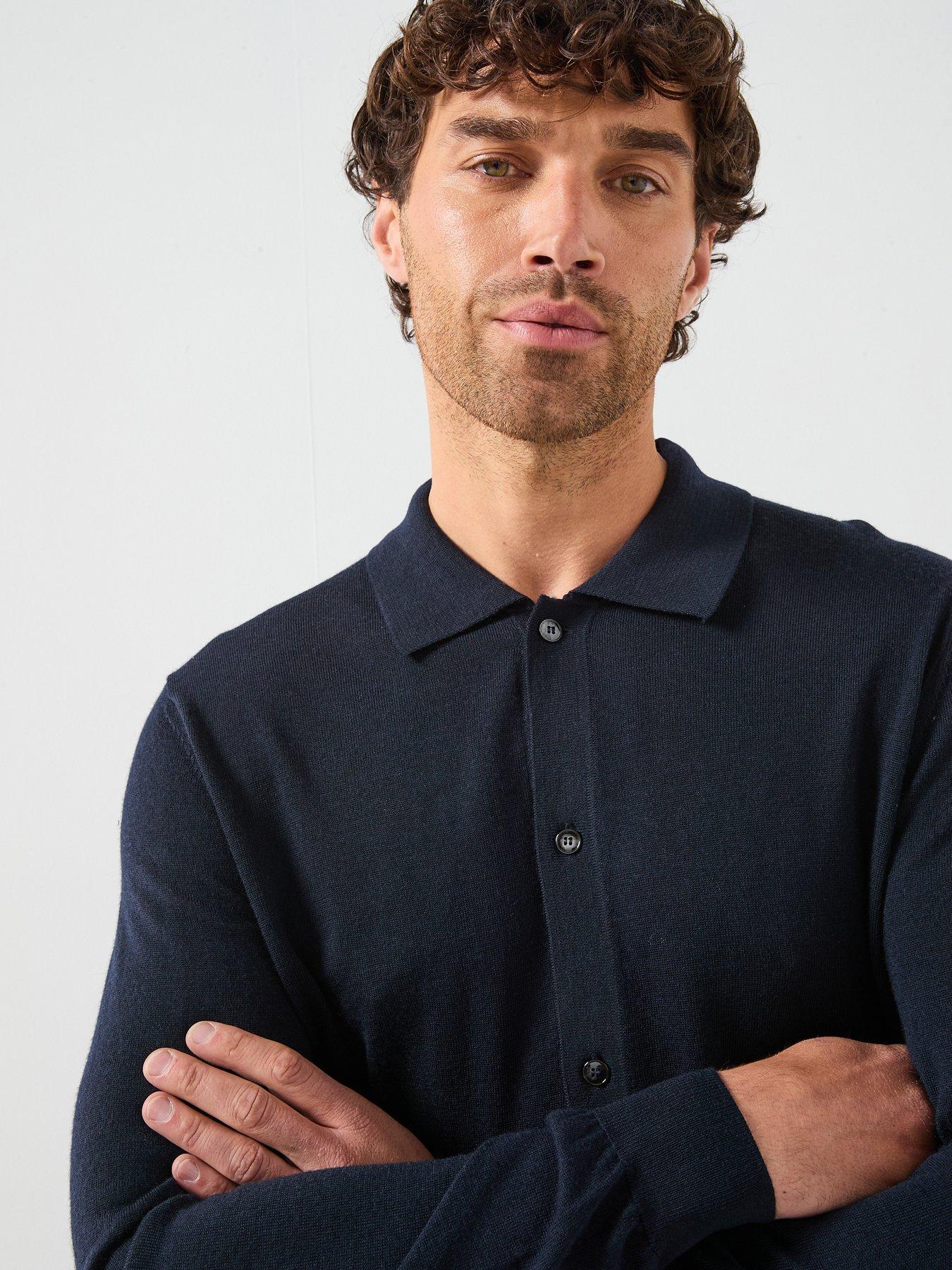 Model poses with his arm crossed showing off the navy blue knitted polo shirt that he's wearing.