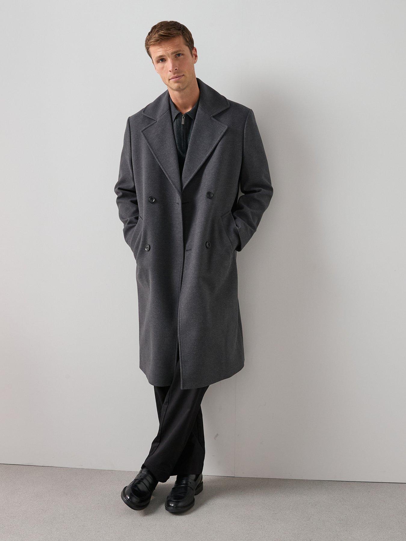 Man poses wearing an oversized grey overcoat - the perfect statement layer for a man's christmas party outfit.