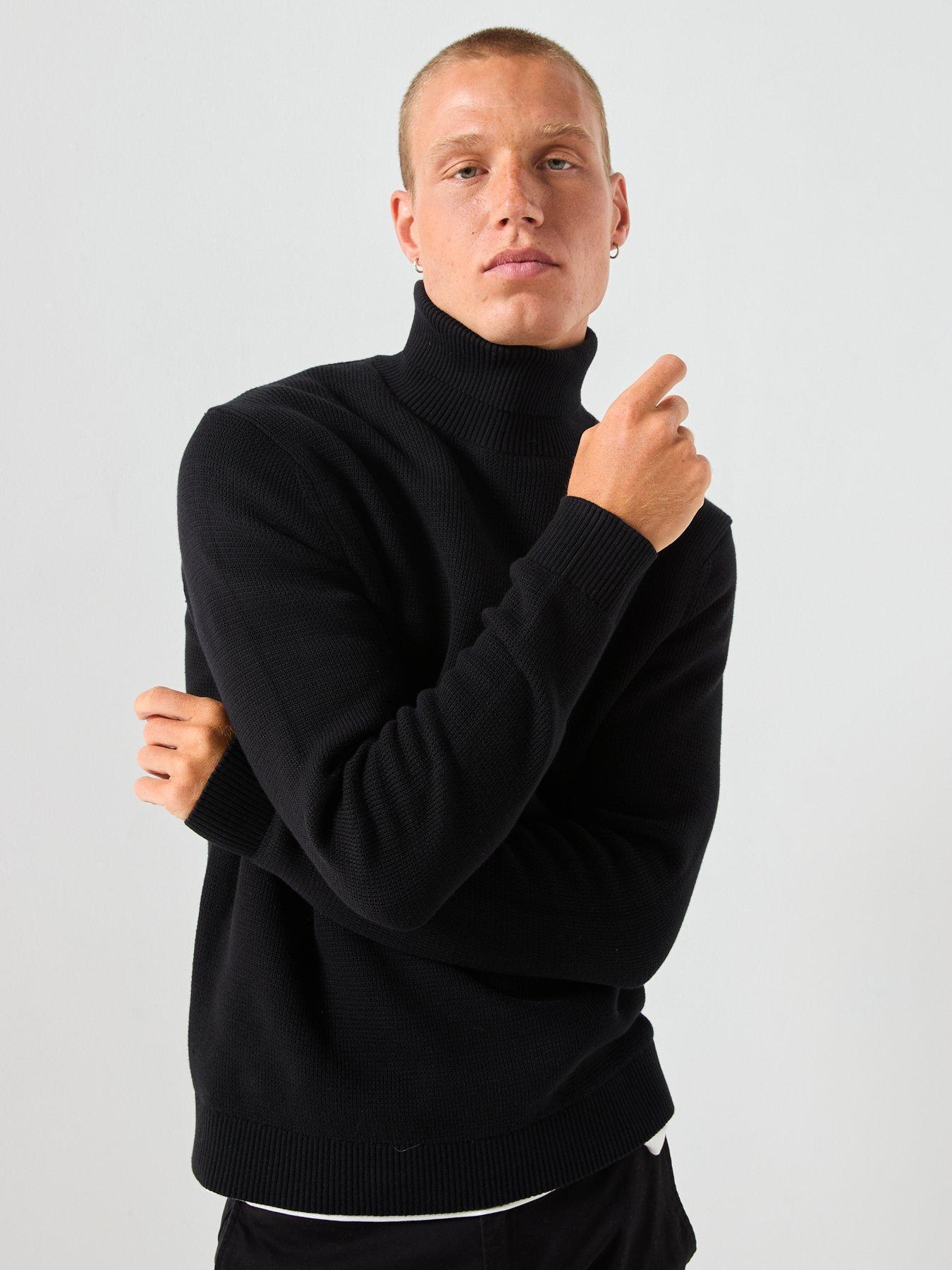 Male model poses showing off the plain black turtle neck jumper he is wearing.