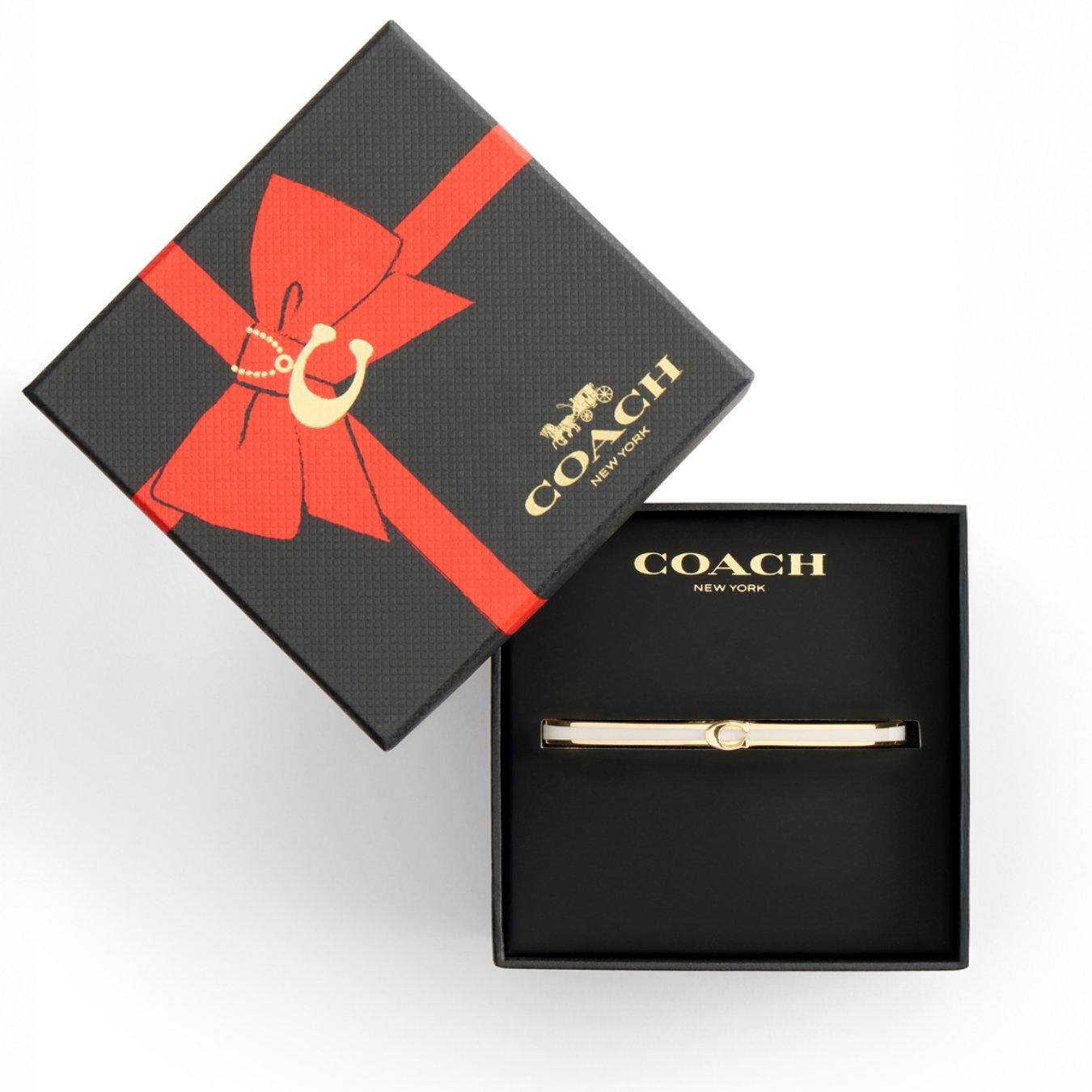 Image of an open box displaying the Coach Bracelet Enamel C Bangle which is gold with the C logo clearly displayed 