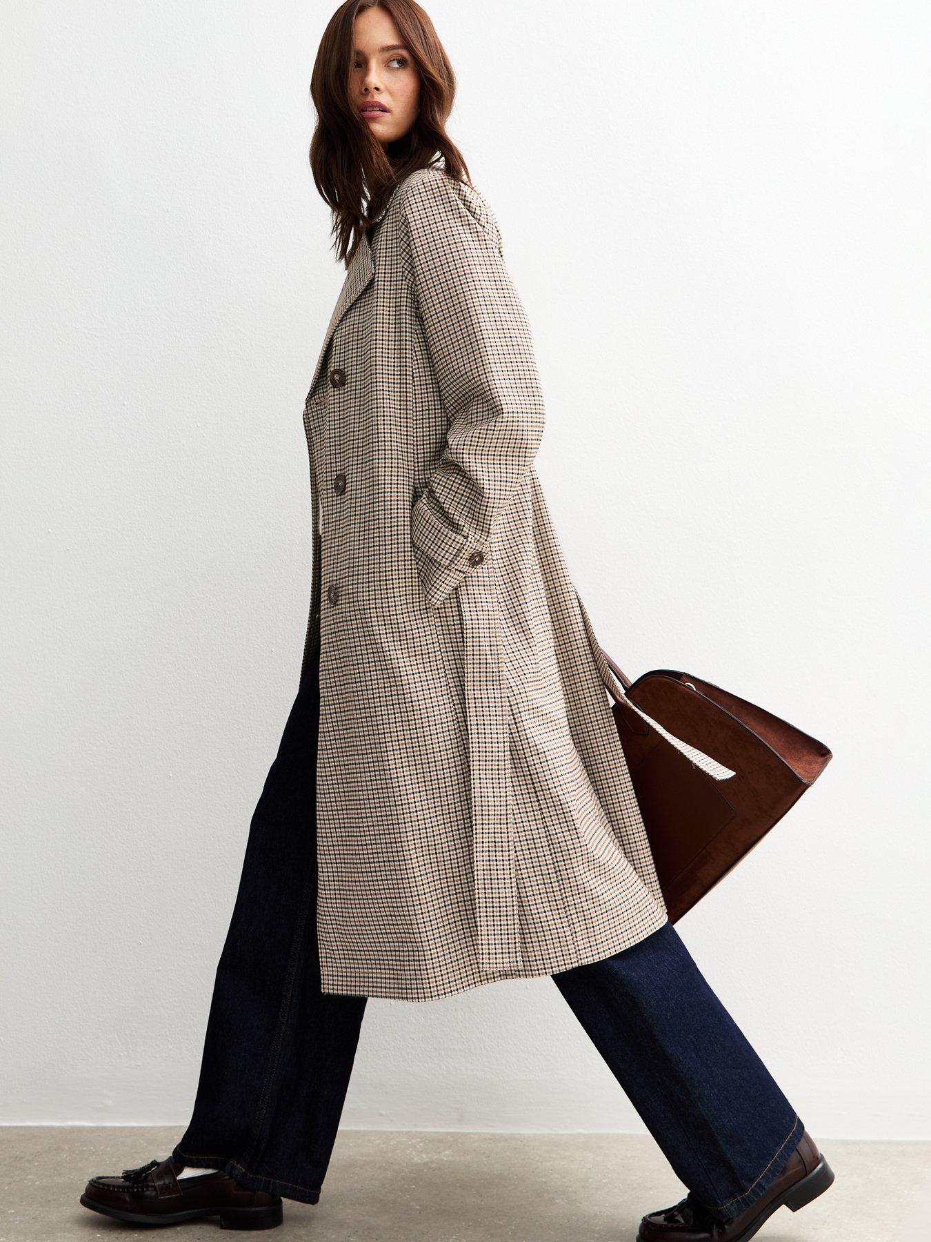 Woman mid-stride wearing a long check trench coat which flows open as she walks