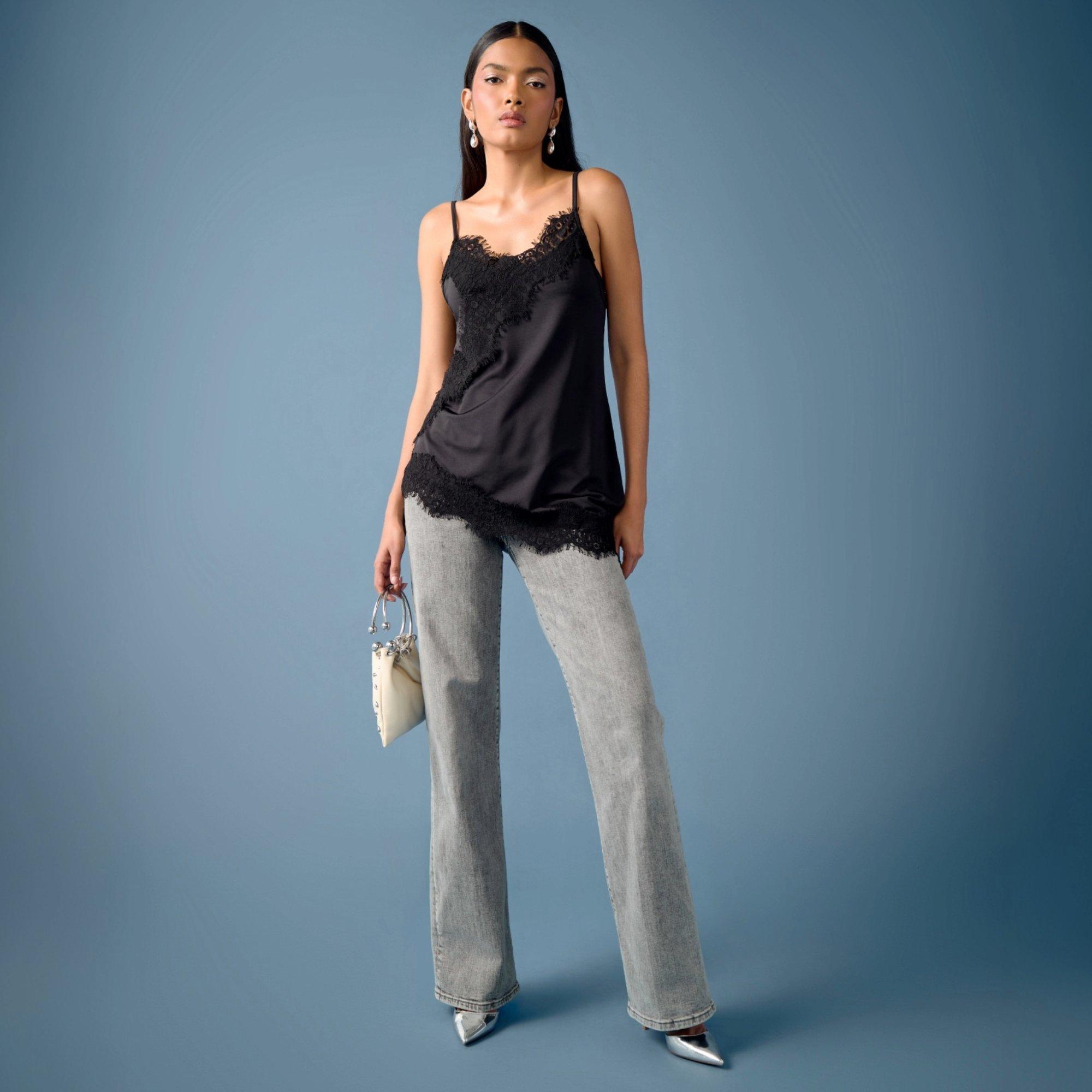 Model poses wearing a pair of straight light wash jeans with a longline lace camisole over the top. The first date ready outfit is finished with a pair of pointy silver heels and matching bag.