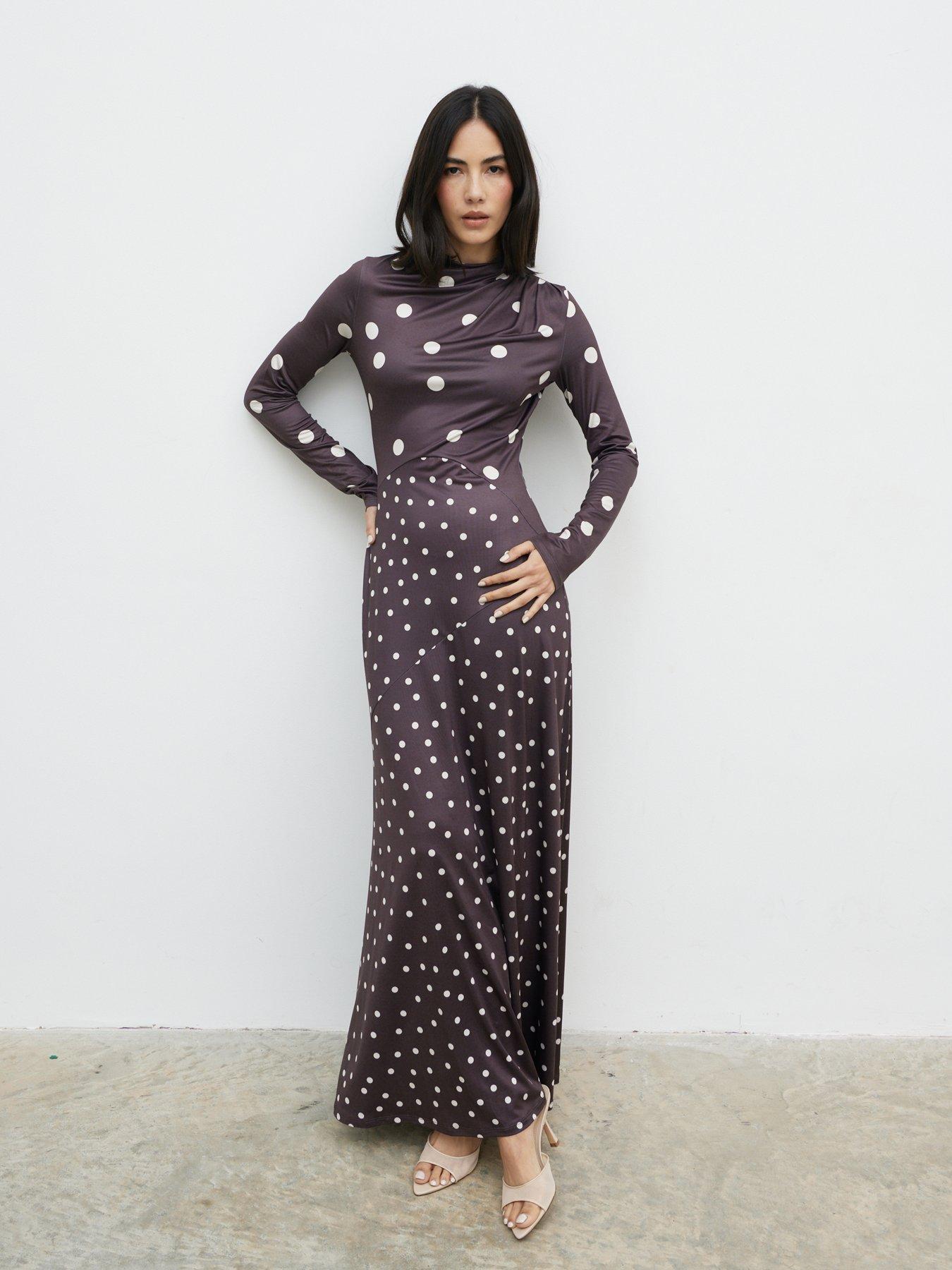 Model poses wearing a long maxi satin polka dot dress. The dress is paired with a pair of heeled sandals.