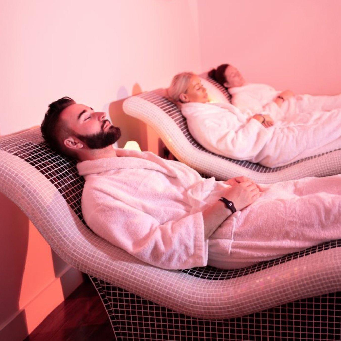 A man and two women in white dressing gowns relaxing on some spa chairs. 