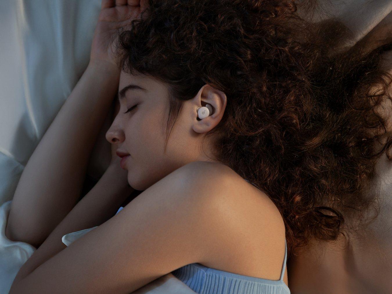 A woman sleeps on her side in bed while wearing Soundcore Sleep A20 Earbuds.