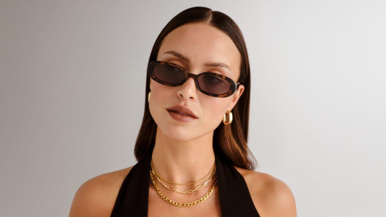A woman with a square shaped face wearing a pair of flattering small oval shaped sunglasses in brown